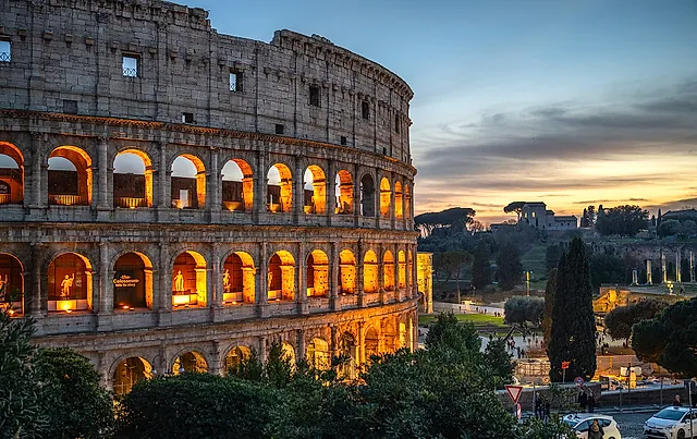 The Colosseum at dusk, with its arches lit from inside and a pale evening sky behind
